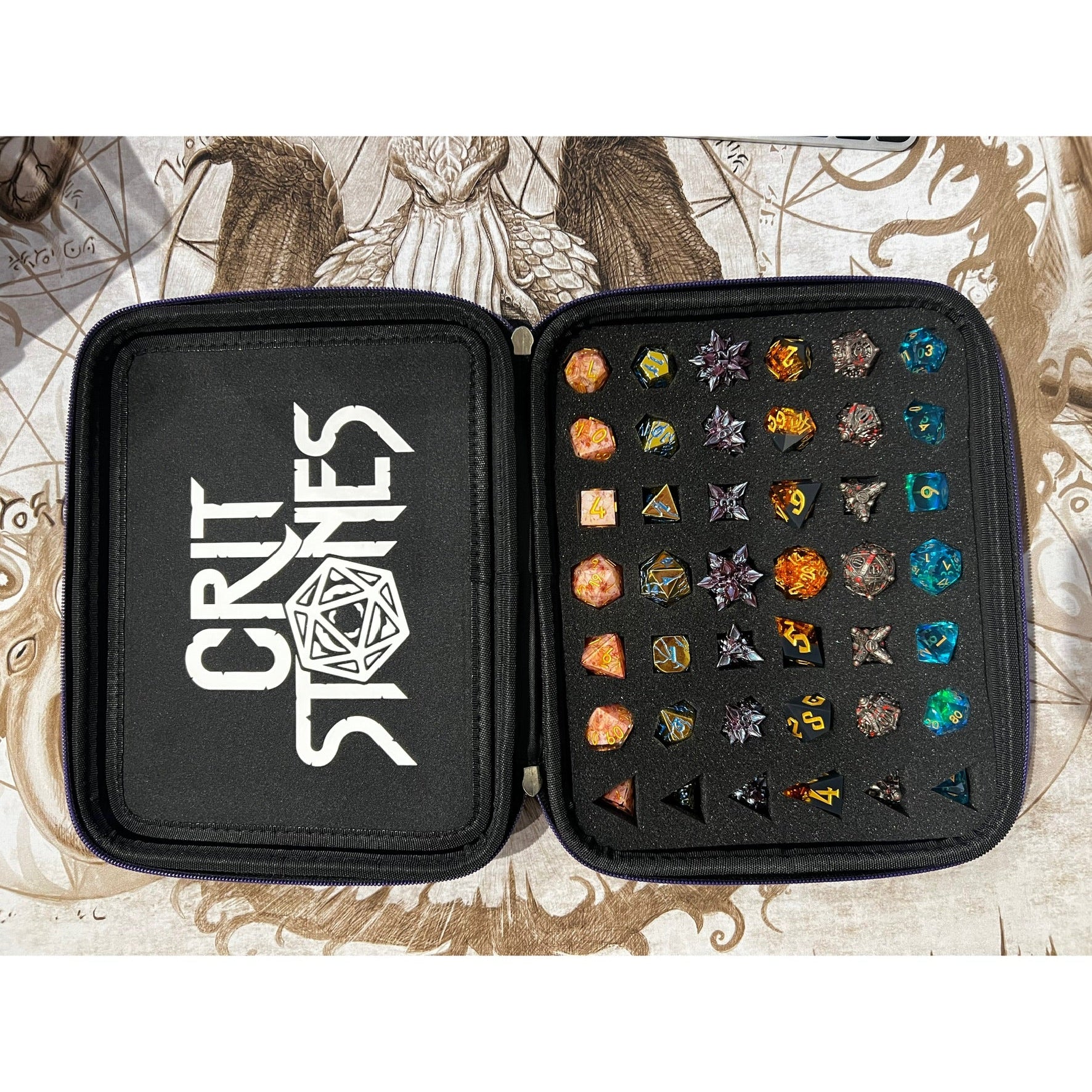 Zwart etui met 'Crit Stones'-logo met daarin verschillende kleine dobbelstenen op een achtergrond met fantasiethema